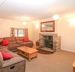A living room with a sectional sofa red cushions a wooden coffee table stone fireplace and mirror at The Old Barn in Harman's Cross near Swanage