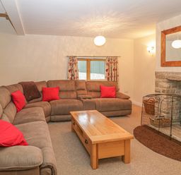 A living room with brown sectional sofa red cushions wooden coffee table and fireplace at The Old Barn in Harman's Cross near Swanage