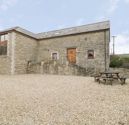Stone building with steps leading to a wooden door and a picnic table on a gravel area at The Old Barn in Harman's Cross near Swanage