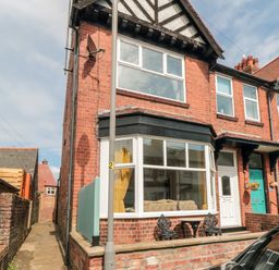 A red brick end terrace house with bay window yellow curtains and black metal chairs on the front patio at The Robins in Filey
