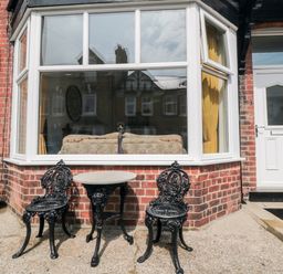 A brick exterior with two black metal chairs and a small round table in front of a large window at The Robins in Filey