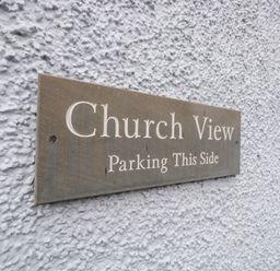 A close-up of a metal sign on a textured white wall reading Church View Parking This Side