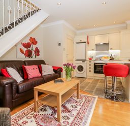 An open plan living room and kitchen with a brown leather sofa and red stools at Church View in Ambleside