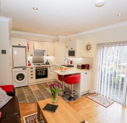 A kitchen and living area with white cabinets red bar stools and a coffee table with flowers at Church View in Ambleside