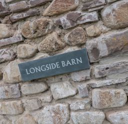 A stone wall with a plaque reading Longside Barn in Gilwern