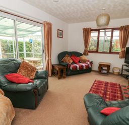 A living room with green leather armchairs a sofa a television and sliding glass doors leading to a conservatory at Bryn yr Haf in Llanfair Clydogau near Lampeter