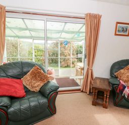 A living room with green leather armchairs with cushions and a small wooden table near sliding glass doors opening to a garden at Bryn yr Haf in Llanfair Clydogau near Lampeter