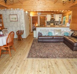A living room with a brown leather sectional sofa and a dining table with wooden chairs at Y Caban in Llechwedd The Conwy Valley