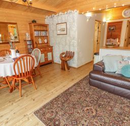 A wooden dining area with table and chairs next to a brown leather sofa and hallway at Y Caban in Llechwedd The Conwy Valley