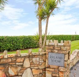 A stone wall with a sign reading Island View beside a trimmed hedge and palm trees at Island View in Ardmore County Waterford