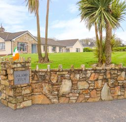 A stone wall with an island view sign and an Irish flag in front of a house with palm trees at Island View in Ardmore County Waterford
