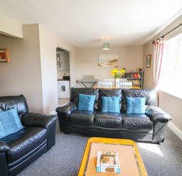 A living room with black leather sofas blue cushions a wooden coffee table and a dining table with flowers at Island View in Ardmore County Waterford