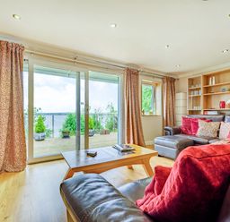 A living room with leather sofas and red cushions near sliding glass doors with patterned curtains at Solway Cottage in Bowness-on-Solway near Wigton