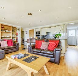A living room with brown leather sofas red cushions a wooden coffee table and an open kitchen with bar stools at Solway Cottage in Bowness-on-Solway near Wigton