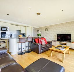 An open plan living area with a kitchen island and bar stools and leather sofas and a wooden coffee table and a television at Solway Cottage in Bowness-on-Solway near Wigton