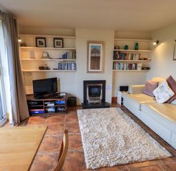 A living room with a sofa and cushions a rug a fireplace shelves with books and a TV at Walkers Retreat in Ambleside