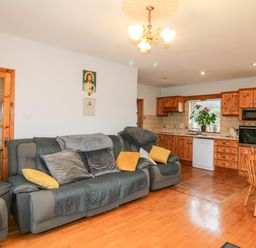 A living area with grey sofas with cushions and a kitchen with wooden cabinets and dining table at Raheen in Castletownshend County Cork
