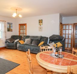 A living room with wooden chairs around a round tiled table and three sofas with cushions at Raheen in Castletownshend County Cork