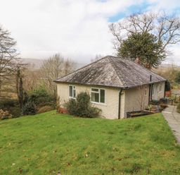 A bungalow with a sloped roof surrounded by grass and trees at Bron Aber in Arthog near Dolgellau