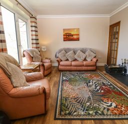 A living room with leather sofas a patterned rug a wood burning stove and striped curtains at Bron Aber Arthog near Dolgellau