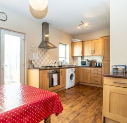 A kitchen with wooden cabinets a washing machine oven microwave and a table with a red polka dot tablecloth at Tomeg in Amble-by-the-Sea