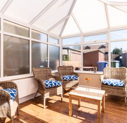 A sunroom with wicker chairs and blue cushions around a wooden table at Tomeg in Amble-by-the-Sea