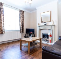 A living room with brown leather sofas a wooden coffee table a flat screen television and a fireplace at Tomeg in Amble-by-the-Sea