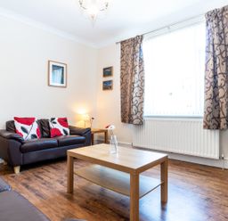 A living room with leather sofas a wooden coffee table a lamp and patterned curtains at Tomeg in Amble-by-the-Sea
