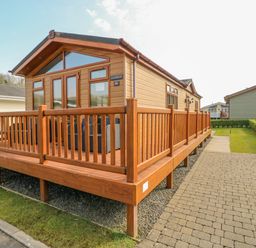 A wooden cabin with a fenced deck and outdoor chairs on a paved and grassy area at Cladebrine Wisemans Bridge near Saundersfoot