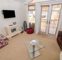 A living room with a wall-mounted TV a glass coffee table and doors leading to a balcony at Cladebrine Wisemans Bridge near Saundersfoot