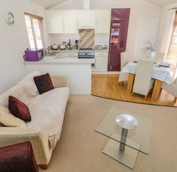 A living room with a sofa pillows glass coffee table and an open kitchen and dining area at Cladebrine Wisemans Bridge near Saundersfoot