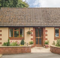 A bungalow with a tiled roof windows and a wooden door with plants in front at Pipistrelle Lodge in Plymtree