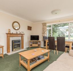 A living room with a fireplace a coffee table a TV and dining table with chairs at Pipistrelle Lodge in Plymtree