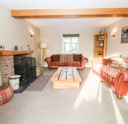 A living room with two sofas a wooden coffee table and a brick fireplace at Ty Top in Llanfaethlu