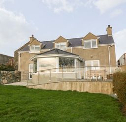 The exterior of a two-story house with a grass lawn and a patio with a wooden bench at Ty Top in Llanfaethlu