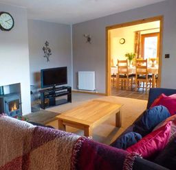 A living room with a wooden coffee table a television a fireplace and a sofa with cushions next to a dining room at Tynddol Bungalow in Llanbadarn-Fynydd near Llanbister