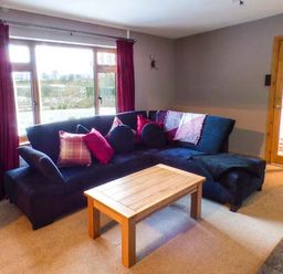 A living room with a dark blue sectional sofa with cushions and a wooden coffee table near a large window at Tynddol Bungalow in Llanbadarn-Fynydd near Llanbister