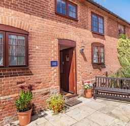 Exterior of a brick cottage with a wooden door, windows, potted plants and a wooden bench at Punch Cottage Little Glemham near Wickham Market