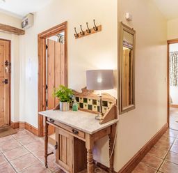 A hallway with a wooden door a wooden table with a lamp and plant and a wall mirror at Punch Cottage in Little Glemham near Wickham Market