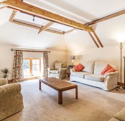 A living room with sofas armchairs a coffee table a TV a window with floral curtains and wooden ceiling beams at Punch Cottage in Little Glemham near Wickham Market