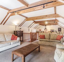 A living room with sofas a wooden coffee table exposed ceiling beams and an open kitchen at Punch Cottage in Little Glemham near Wickham Market