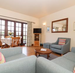 A living room with blue sofas wooden coffee table and dining table near glass doors at Barn Owl Cottage in Little Glemham near Wickham Market