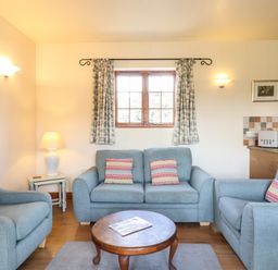 A sitting area with blue armchairs and sofa and a round wooden table in front of a window at Barn Owl Cottage in Little Glemham near Wickham Market