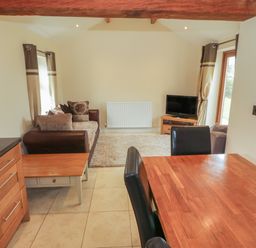 A living room and dining area with a sofa cushions television wooden table and black chairs at Y Beudy Cottage in Clynnog Fawr
