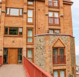 The entrance to a brick and stone apartment building with a red railing pathway and a view of the sea in the background at 37 Ocean Park in Westward Ho