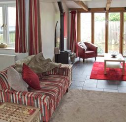 A living room with striped sofas red chair coffee table and large windows at Hour Cottage in Stow-on-the-Wold
