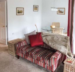 A living room with a striped sofa with cushions and a throw a glass dining table with chairs and framed pictures on the wall at Hour Cottage in Stow-on-the-Wold