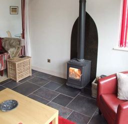 A living room with a wood burning stove a red armchair and a striped sofa at Hour Cottage in Stow-on-the-Wold