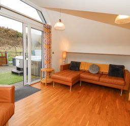 A living room with leather sofas a wooden floor sliding glass doors and a view of an outdoor hot tub at Ty Henri in Tresaith