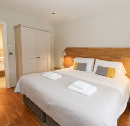 A bedroom with a large bed with folded towels bedside tables and a wardrobe at Ty Henri in Tresaith
